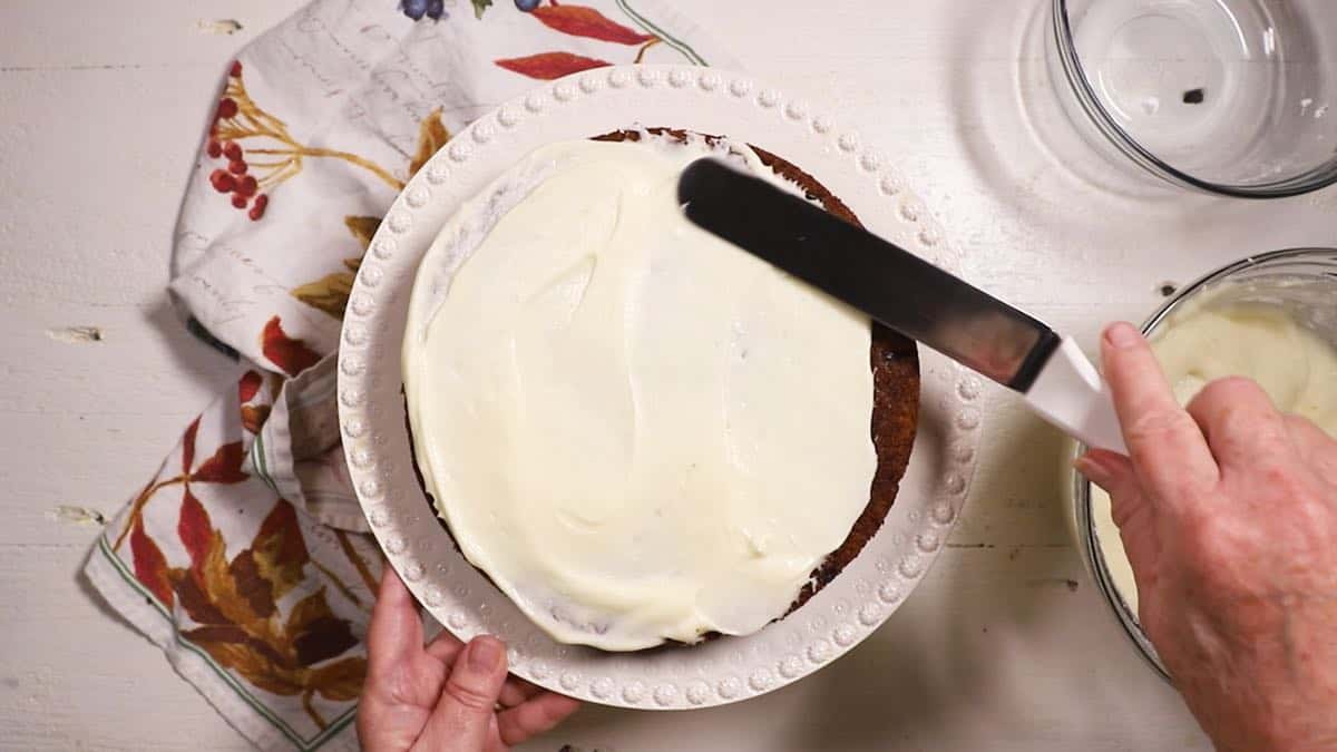 Icing the first layer of a cake on a white cake platter. 