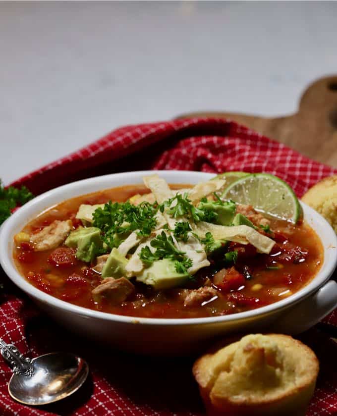 A white bowl full of chicken soup topped with avocado chunks. 