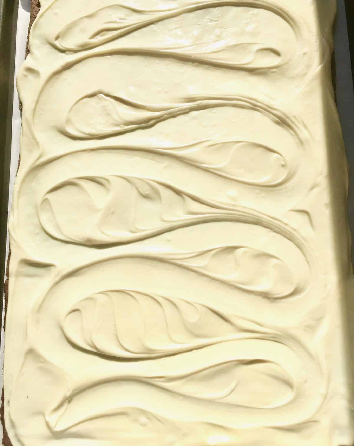 Melted white chocolate spread over graham crackers on a baking sheet. 