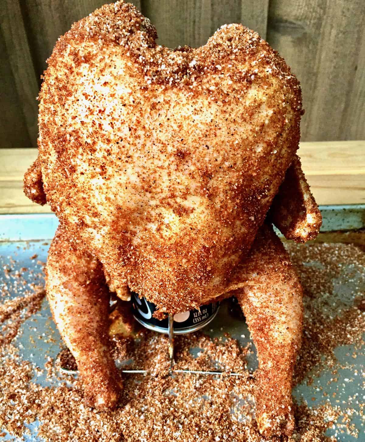 Poultry sitting upright on a beer can covered with a savory rub.