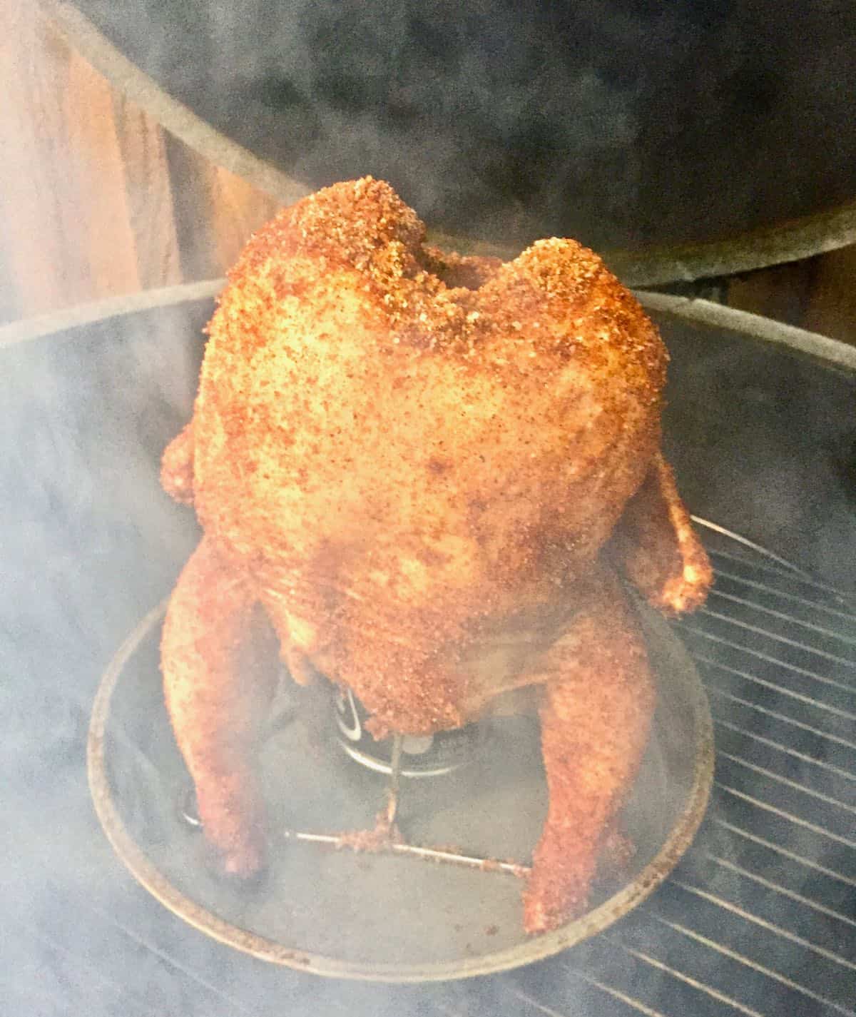 Poultry sitting upright on a grill with smoke rising.