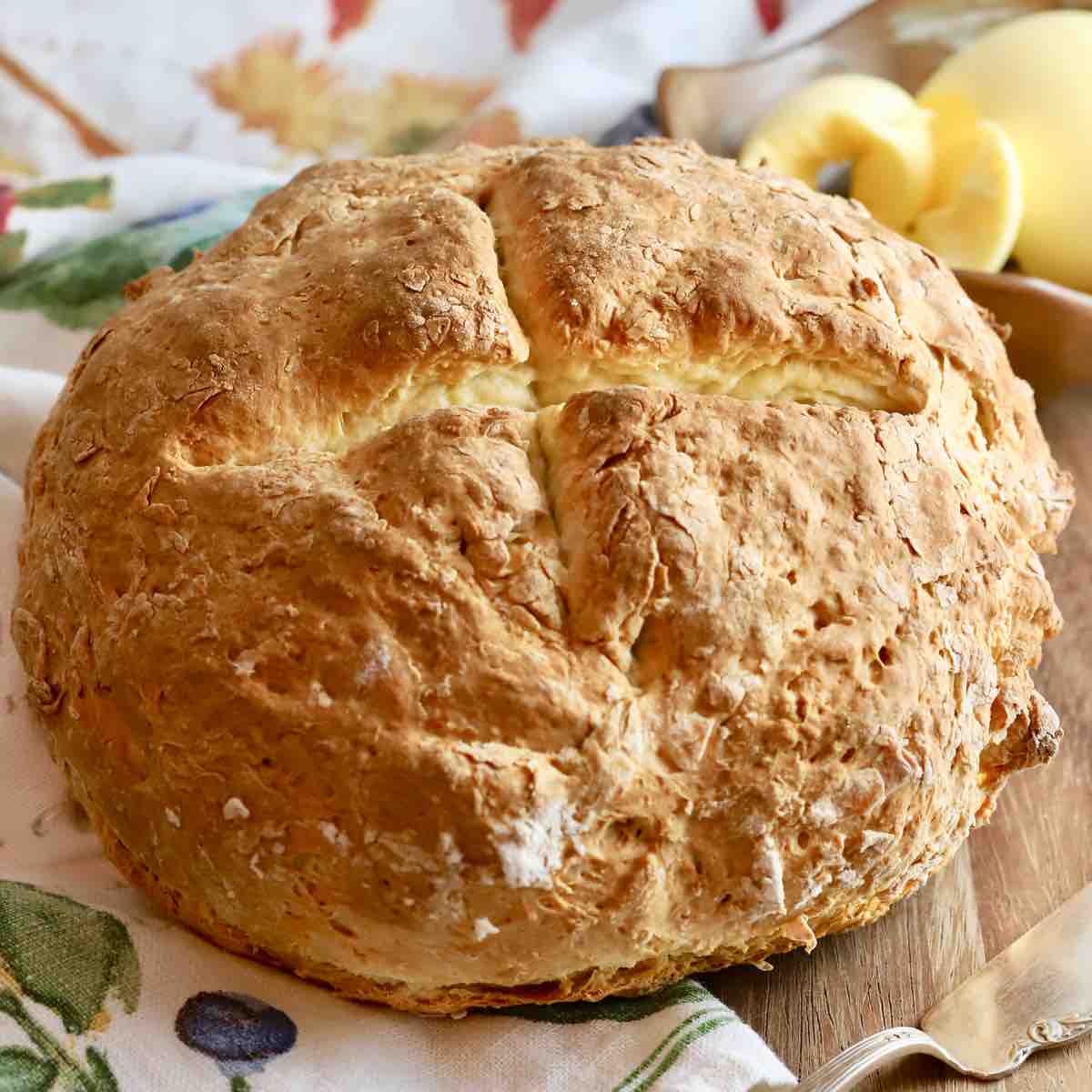 A round of rustic bread on a kitchen towel with a bowl of butter.