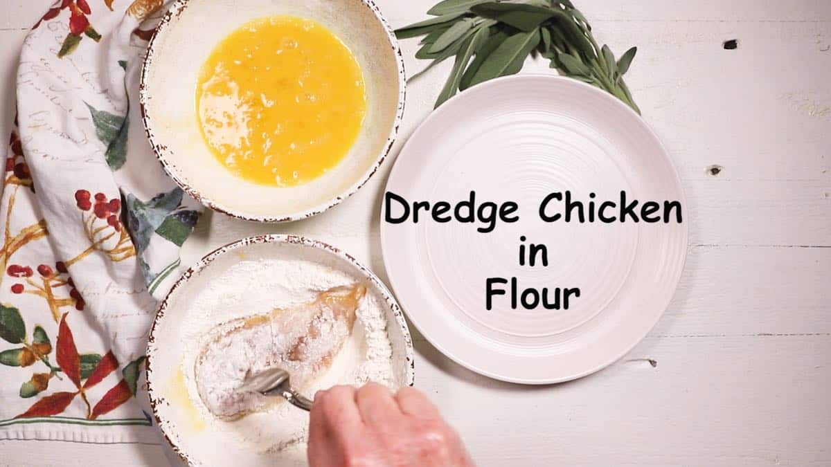 Dredging a chicken breast in flour in a bowl. 