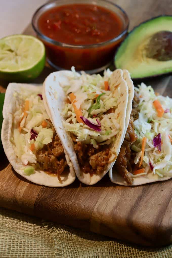 Three pulled pork tacos on a wooden cutting board. 