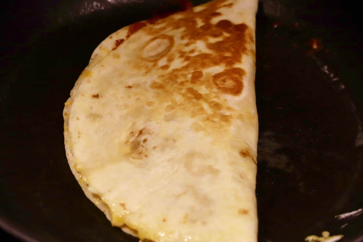 A cooked quesadilla in a black skillat.