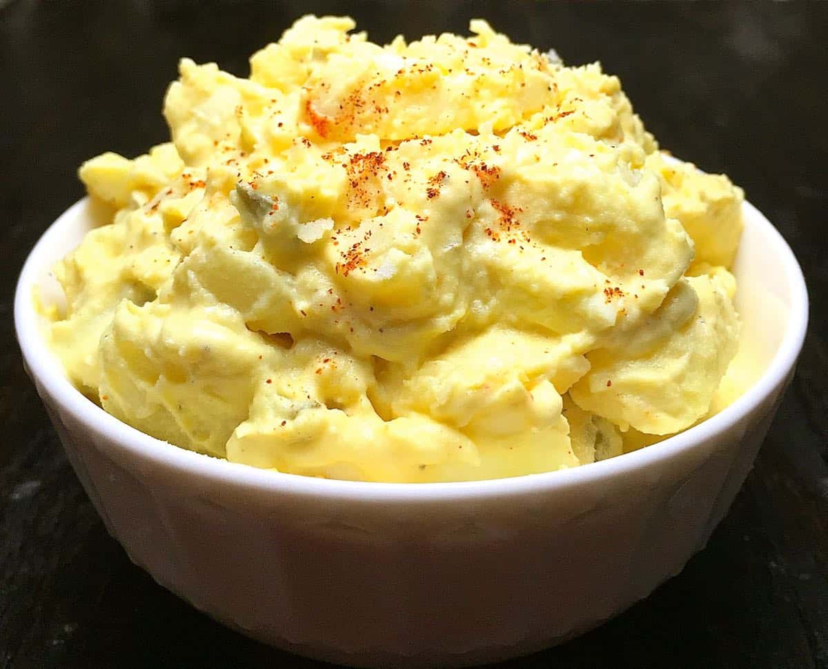 A large bowl of potato salad garnished with paprika.