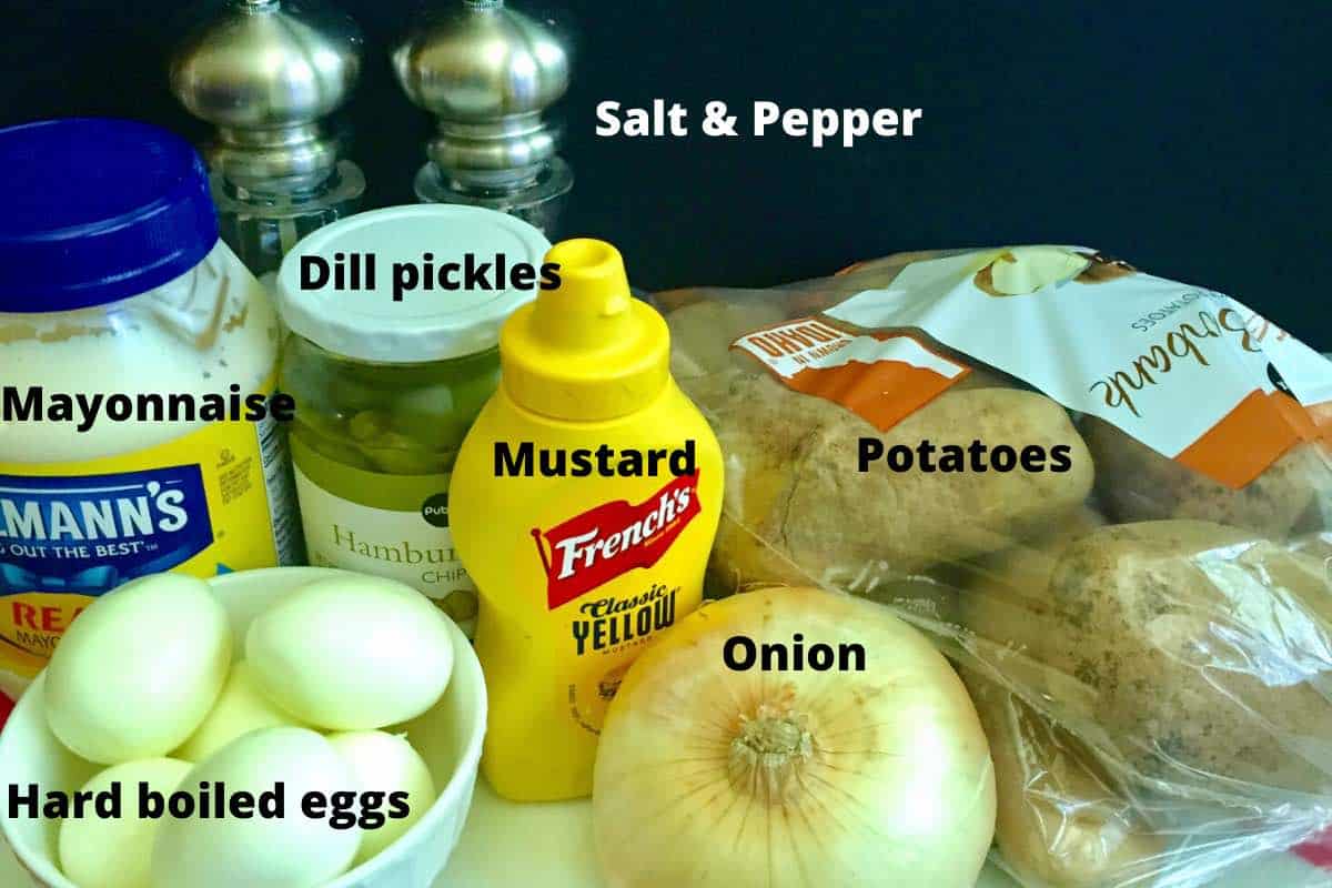 Hard boiled eggs, potatoes, mustard, mayonnaise, and dill pickles on a counter.