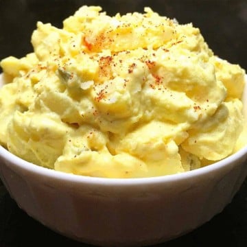 A white bowl full of creamy potato salad topped with paprika.