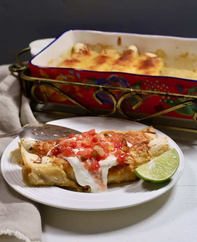 A white plate with two enchiladas topped with salsa and sour cream. 