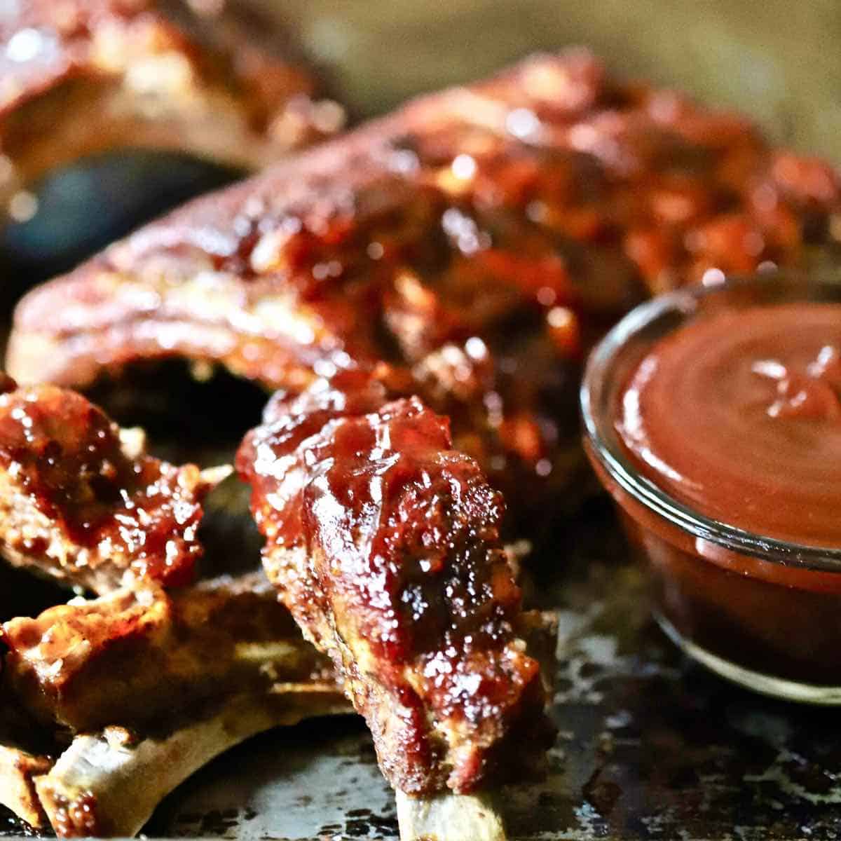 A rack of baby back ribs next to a bowl of barbecue sauce.