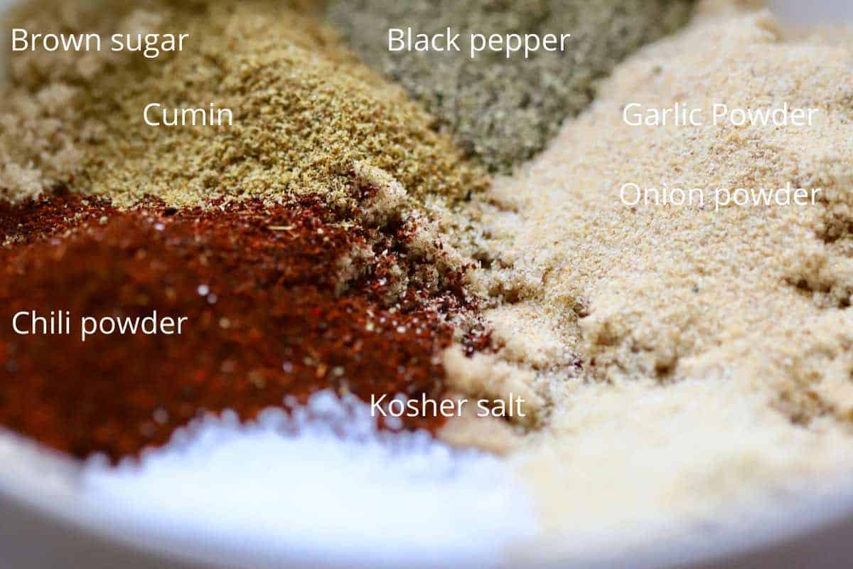 A bowl containing brown sugar, chili powder, cumin, salt, pepper and garlic powder.