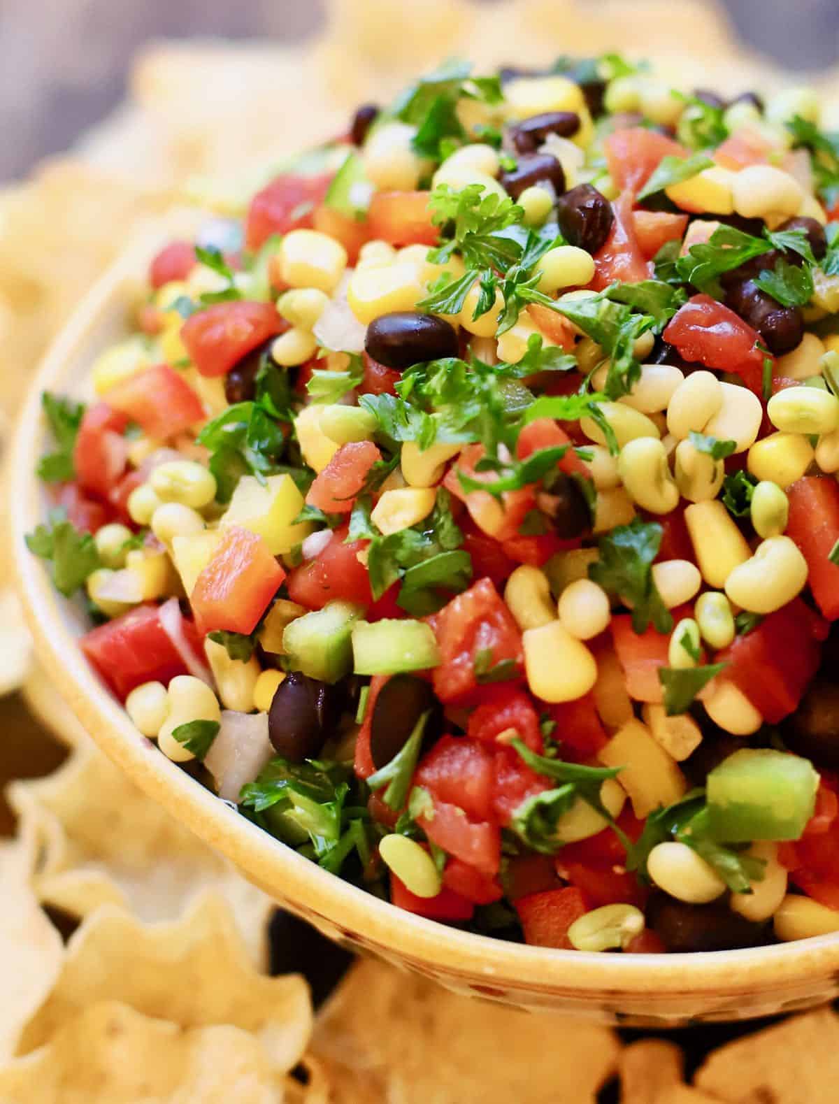 A large bowl full of tomatoes, white acre peas, red and green bell pepper, black beans and garnished with parsley.