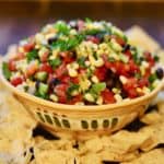A large southwestern looking bowl full of redneck caviar dip surrounded with tortilla chips.