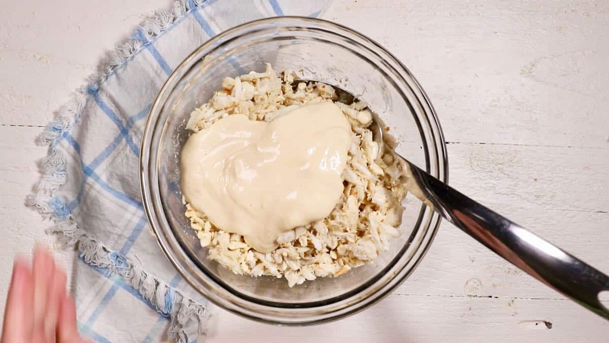 A large clear glass bowl with crab meat, saltines and mayonnaise on top.