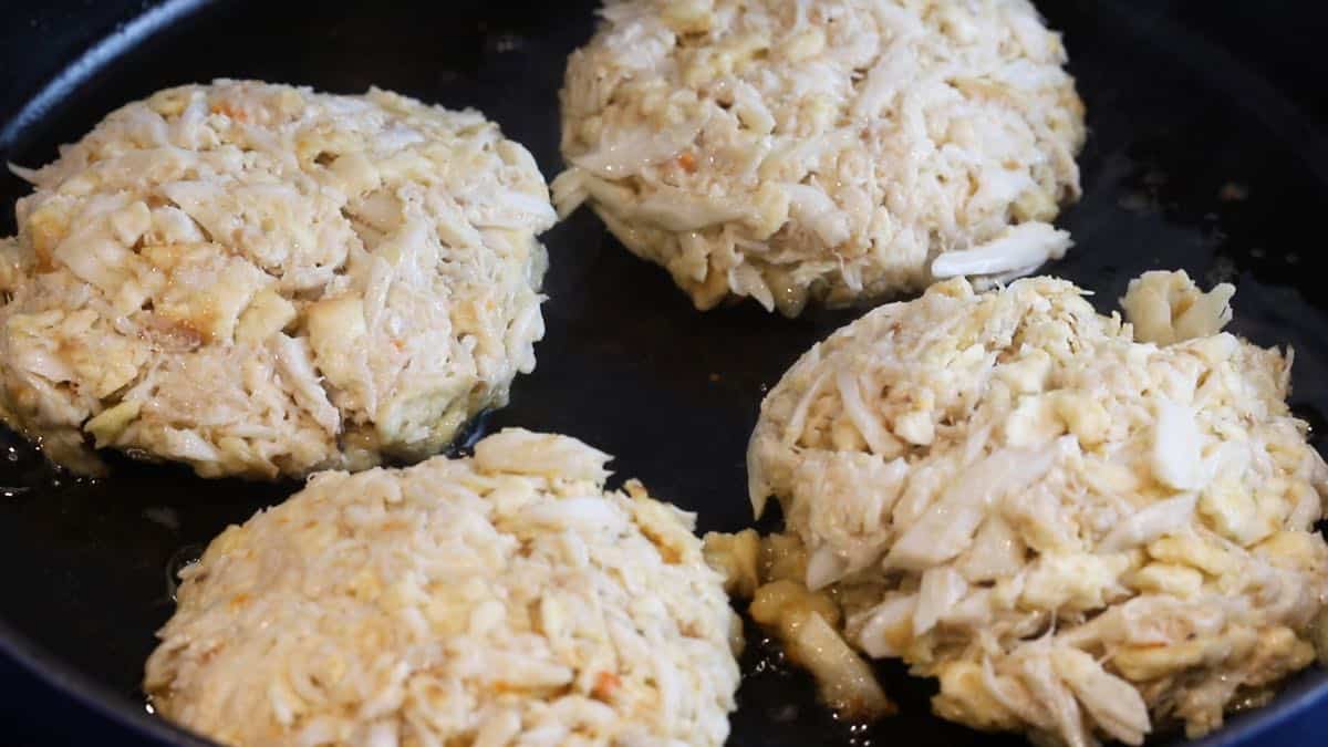 Four crab cakes cooking in a skillet.