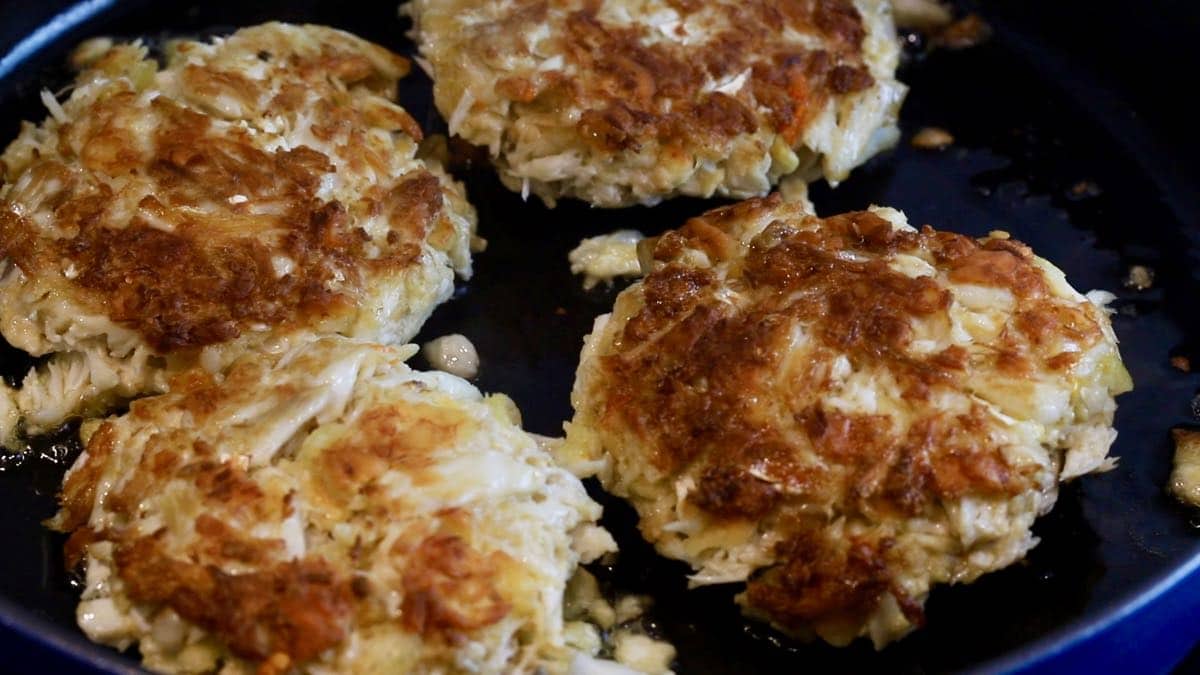 Golden brown crab cakes cooking in a skillet.