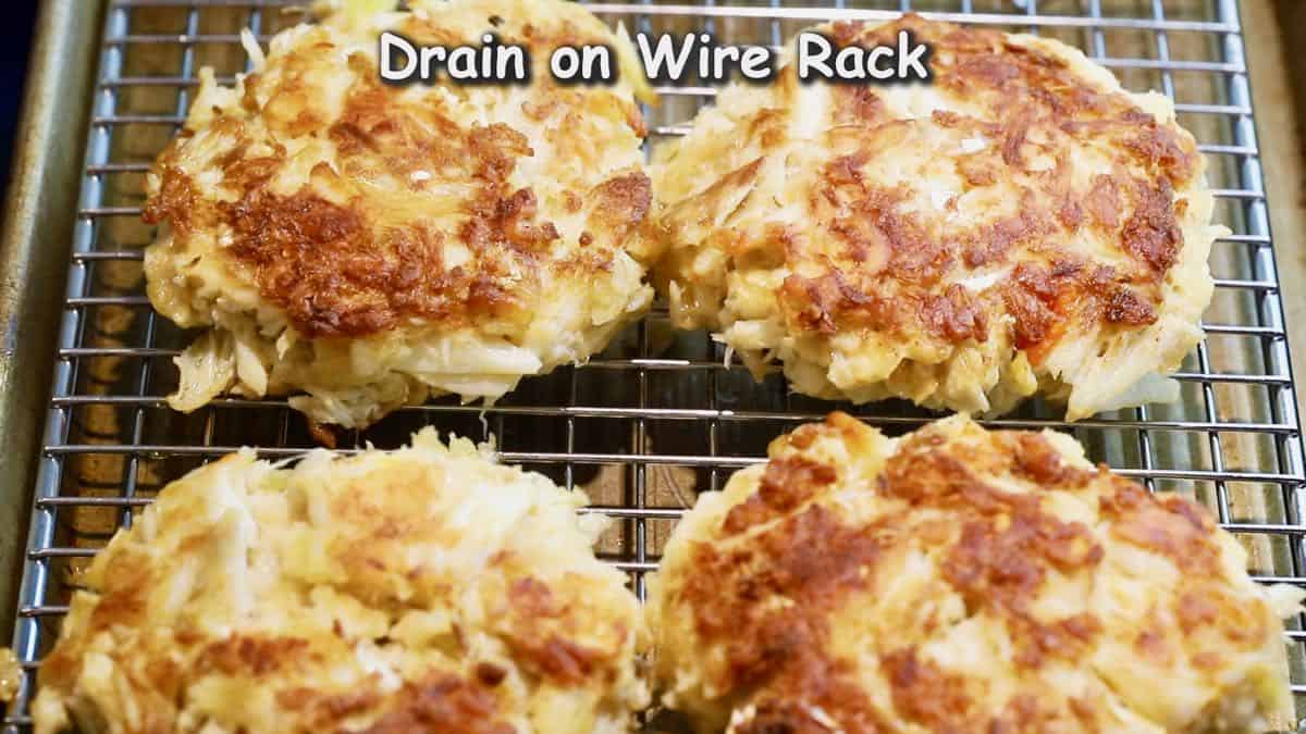 A wire cooling rack with crab cakes just cooked on top.