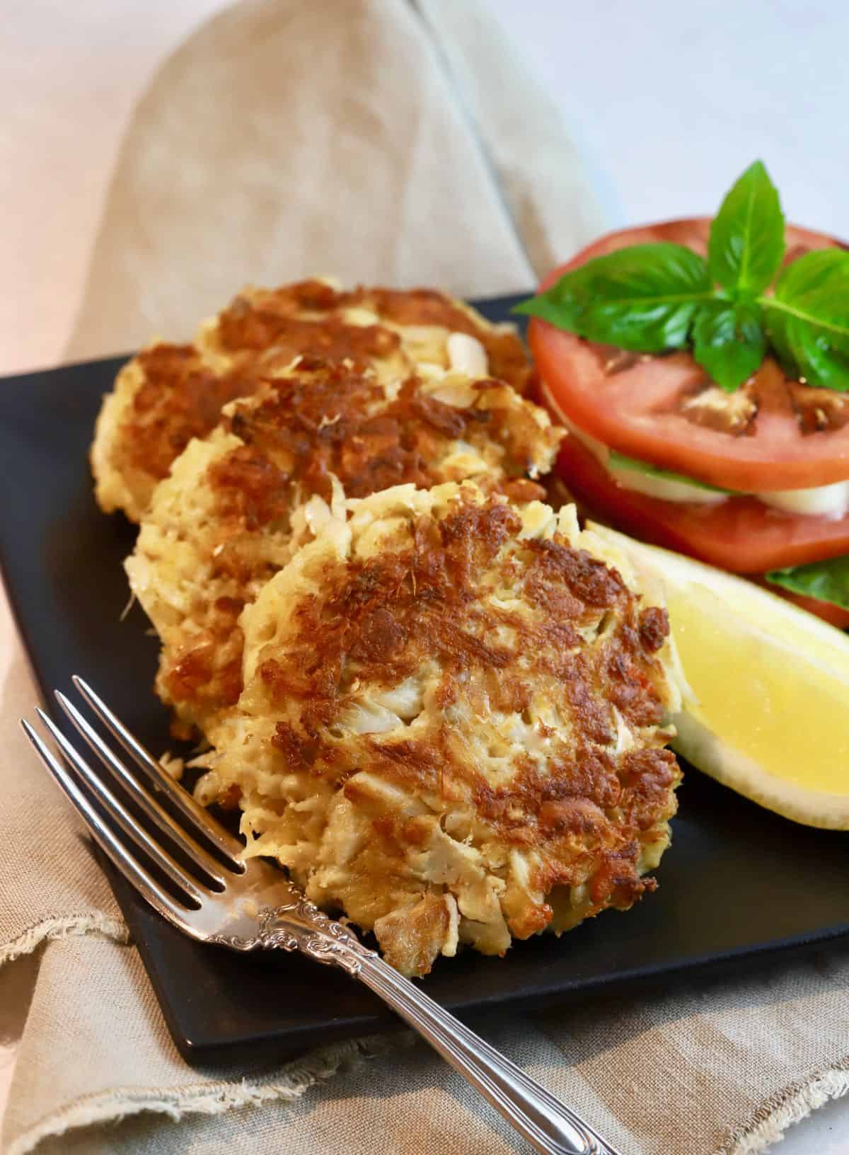 Three crab cakes on a plate with a slice of lemon.