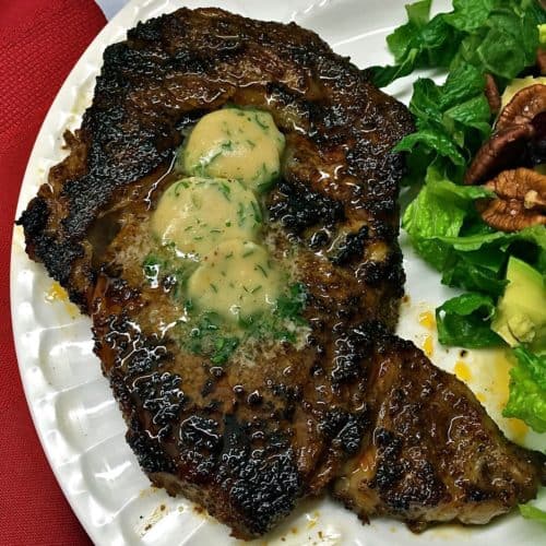 Chili Rubbed Ribeye Steak topped with three pats of Maple Bourbon Butter on a white plate.