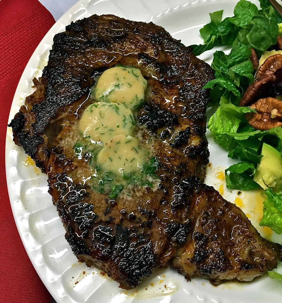 Chili Rubbed Ribeye Steak topped with three pats of Maple Bourbon Butter on a white plate.