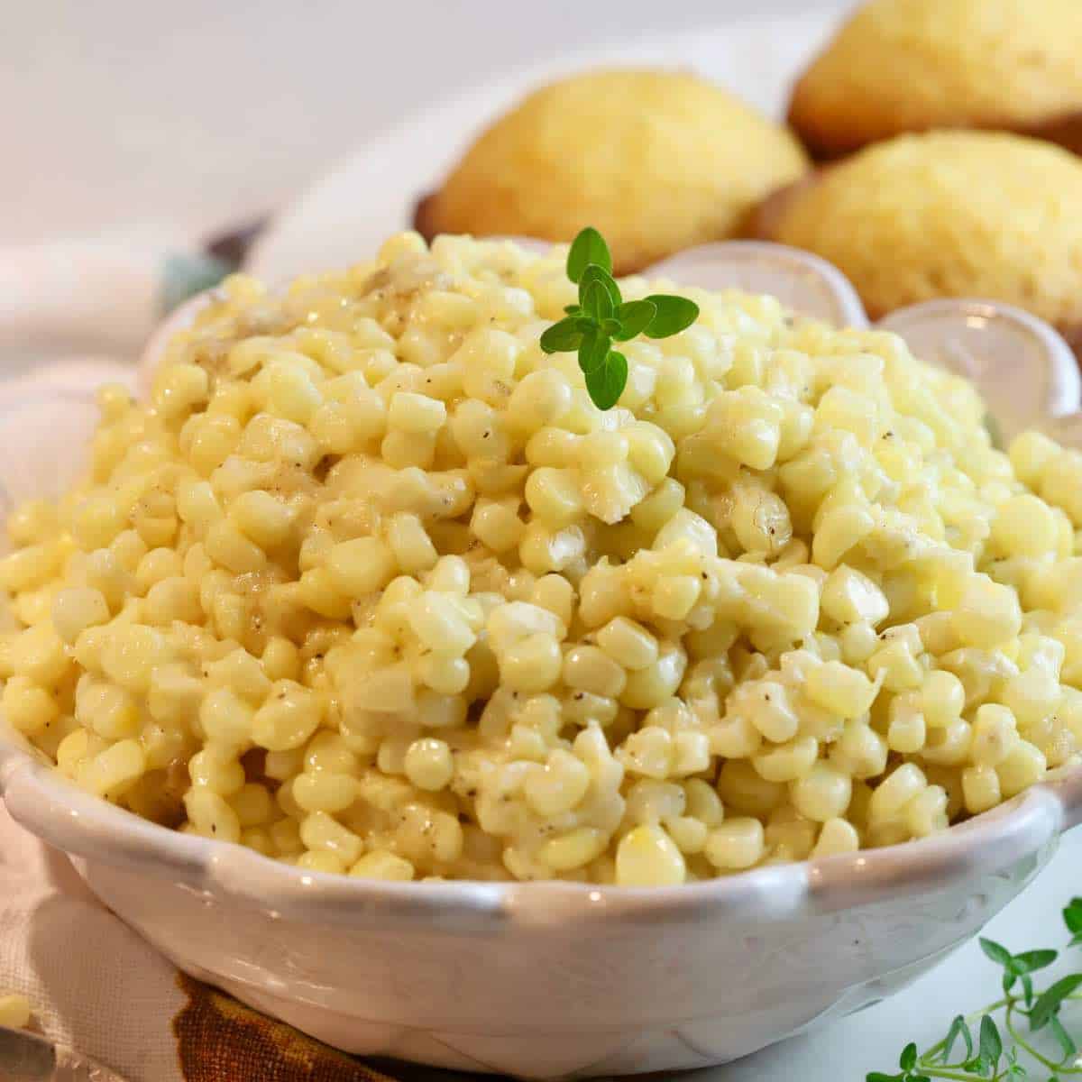 A white bowl full of creamed corn garnished with a sprig of thyme. 