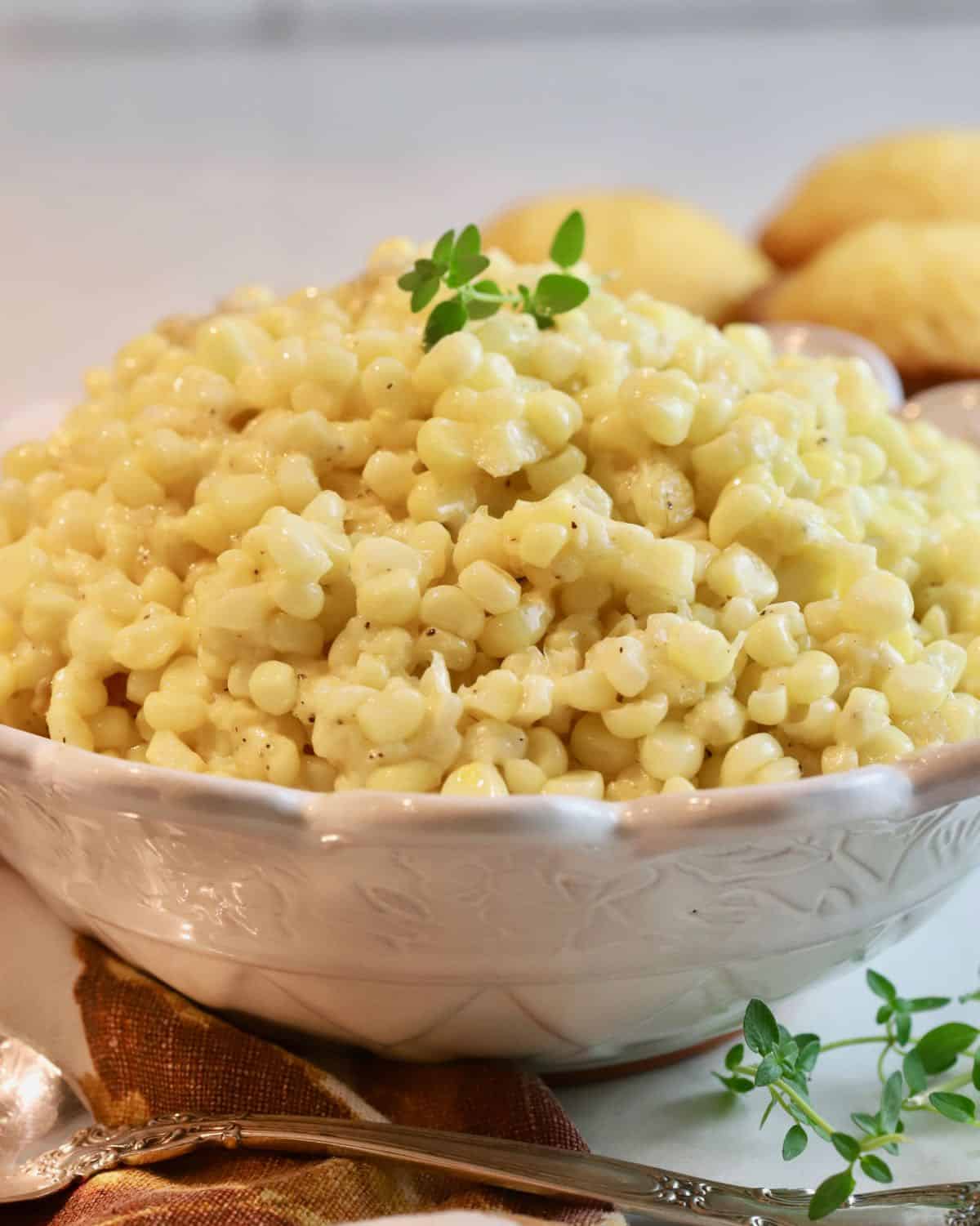 Fresh creamed corn in a white bowl with corn muffins behind it.