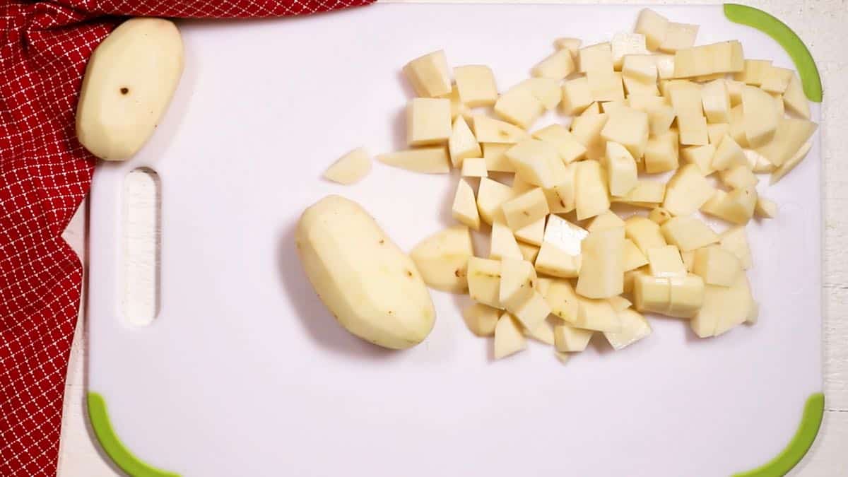 A white cutting board with peeled and cubed potatoes on it.