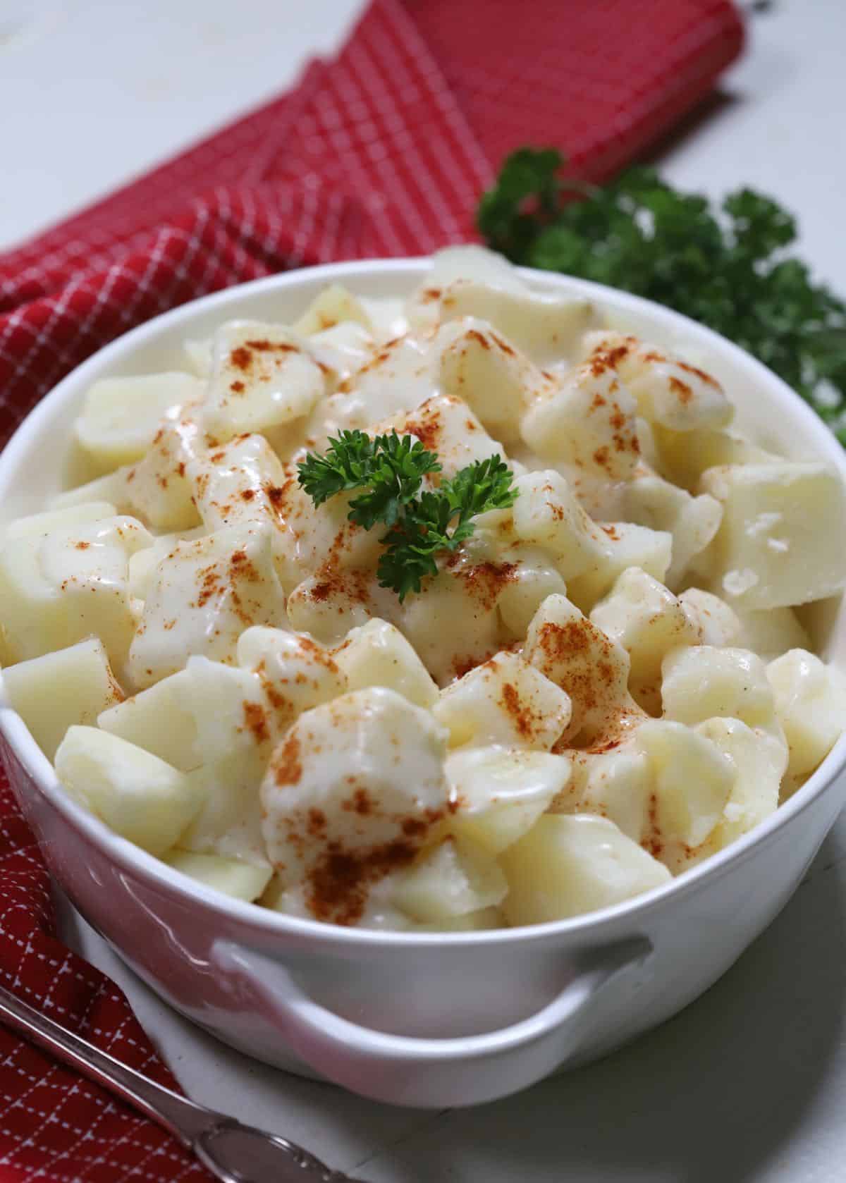 Creamed potatoes in a white serving dish topped with paprika and garnished with parsley. 