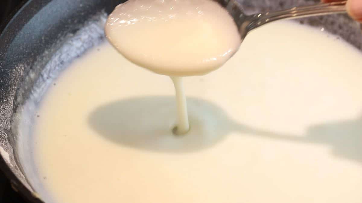 A spoonful of thickened cream sauce in a skillet.