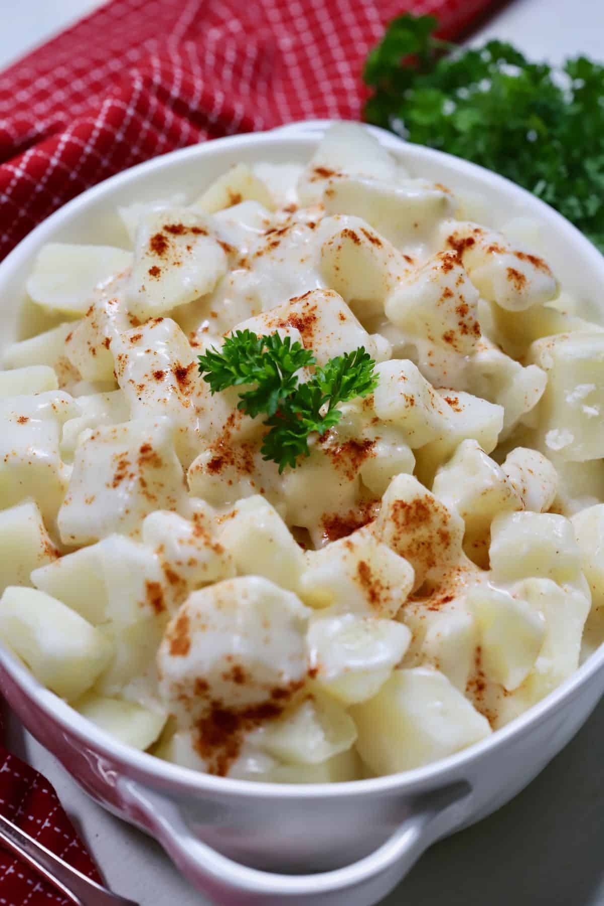 A white oval bowl full of creamed potatoes topped with paprika. 