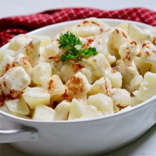 A large white oval bowl full of creamed potatoes and topped with parsley.