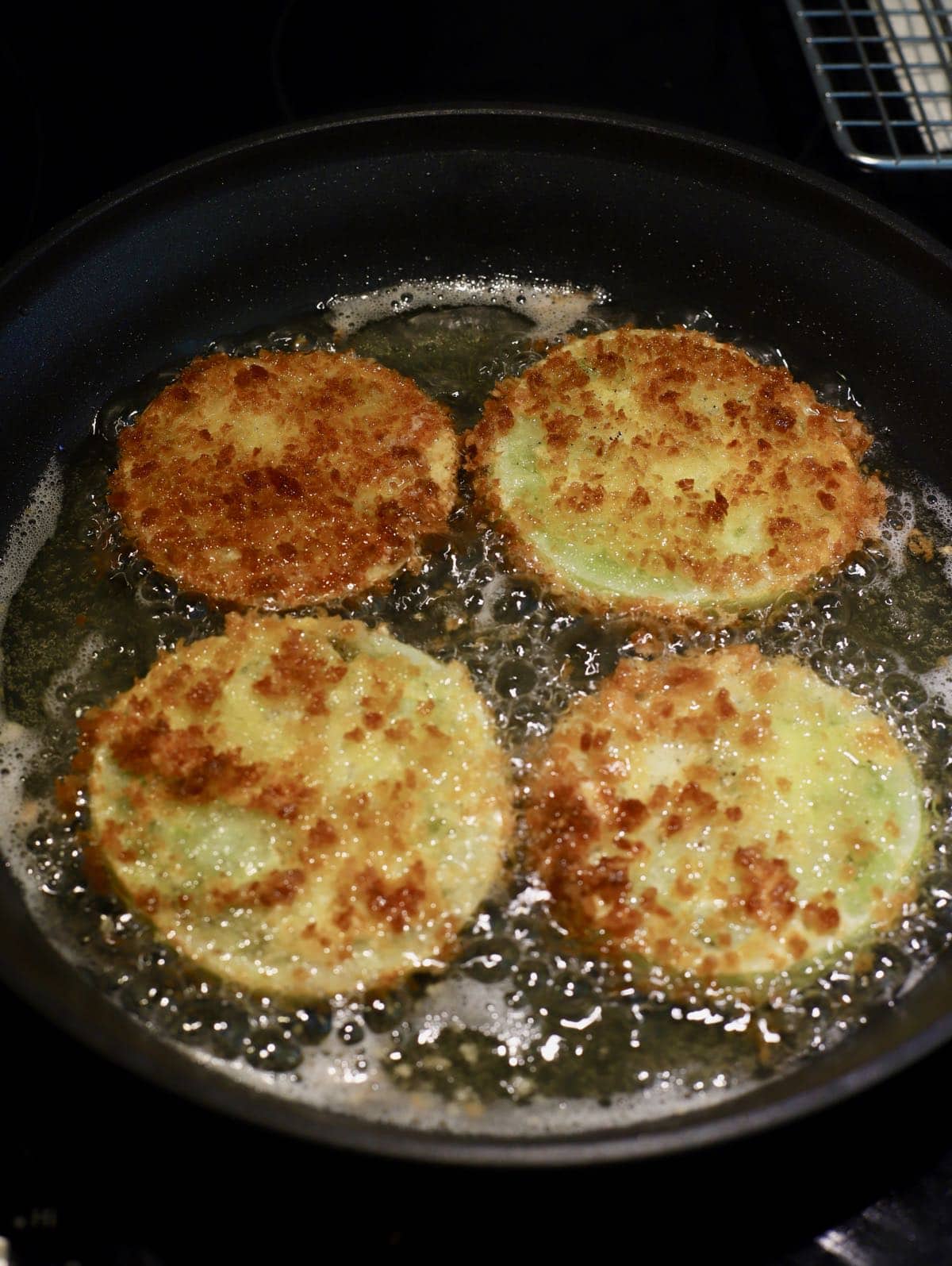 Four tomato slices frying in a large skillet. 