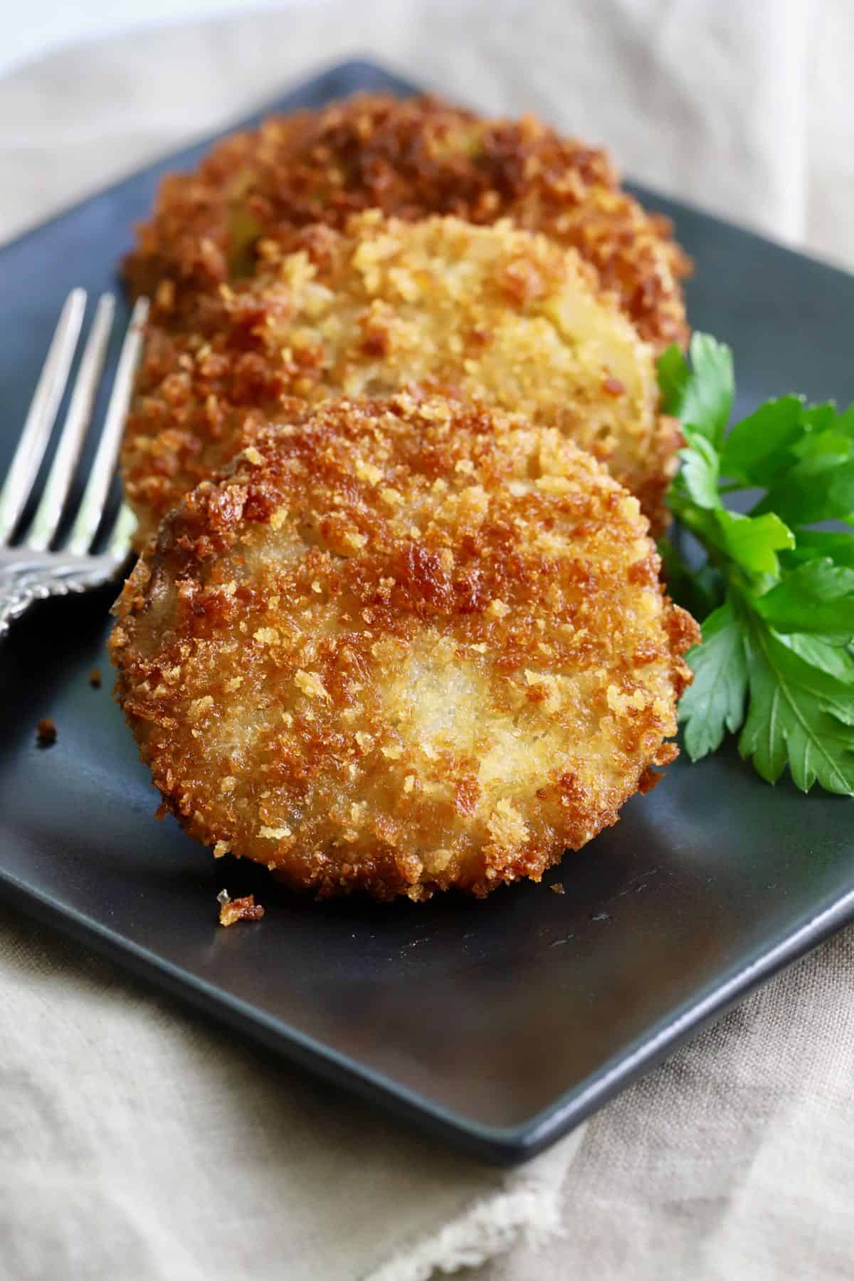 A black plate with three fried green tomato slices on it. 