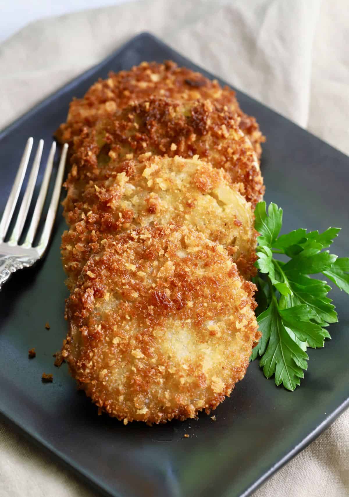 Three fried green tomato slices on a black plate. 