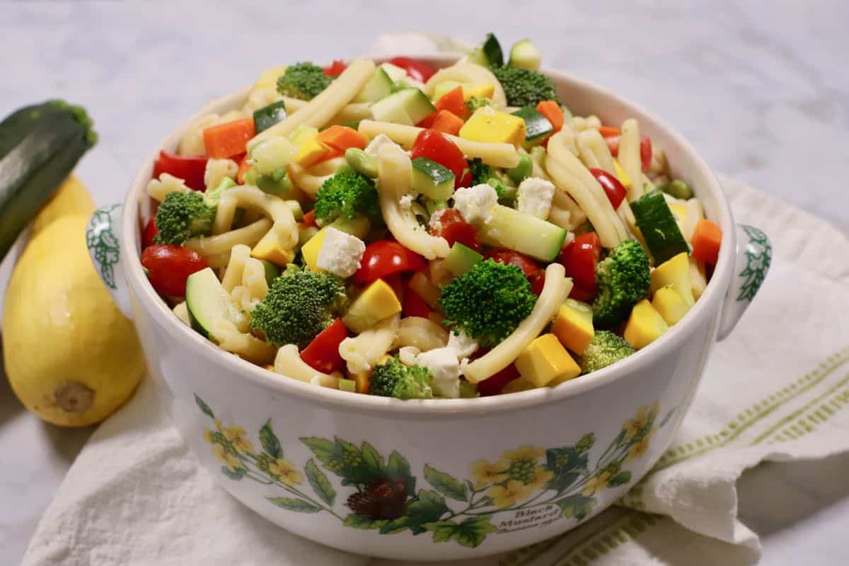 A large bowl with pasta salad topped with broccoli, tomatoes and feta cheese. 