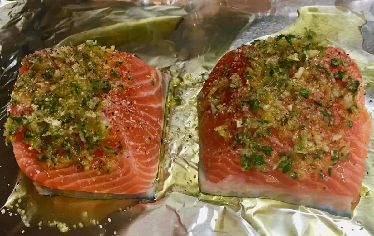 Two salmon fillets topped with herbs on a sheet of aluminum foil.