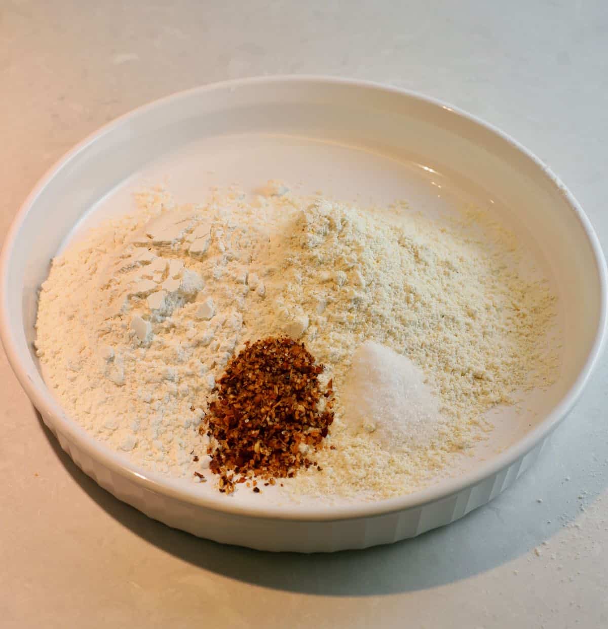 Cornmeal, flour, and Creole seasoning in a white shallow bowl.