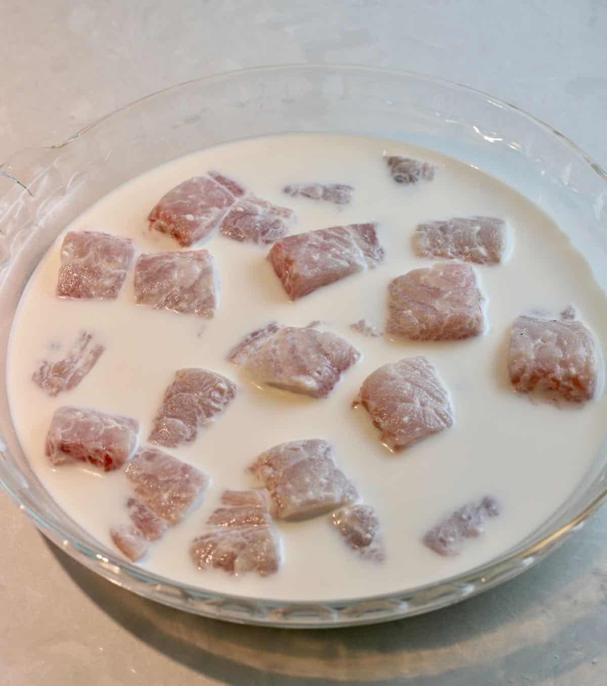 Pieces of fish soaking in buttermilk in a shallow bowl.