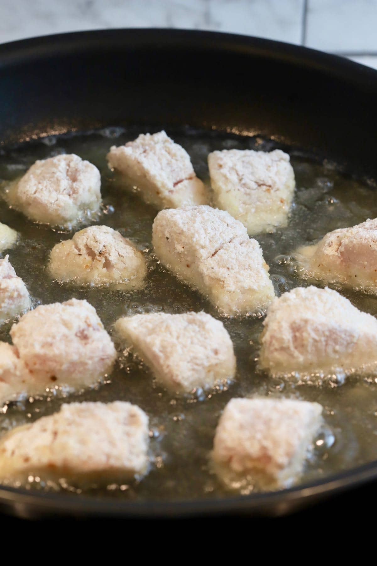 Fish nuggets frying a a black skillet.