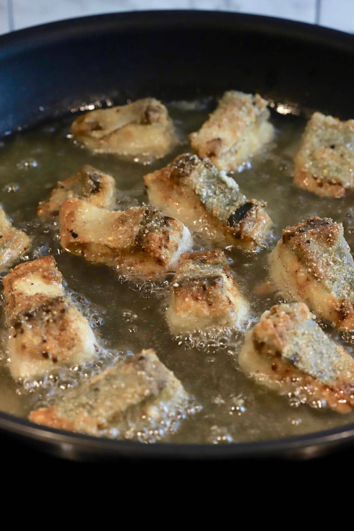 Golden brown fish nuggets frying in a skillet.