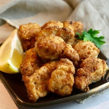 A plate full of Spanish mackerel nuggets with a slice of lemon.