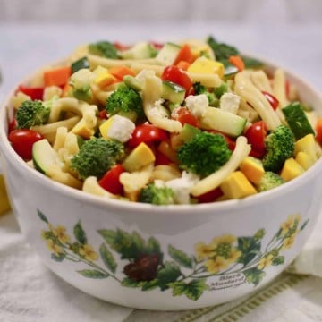 A large bowl with pasta salad and vegetables on a white and green napkin.