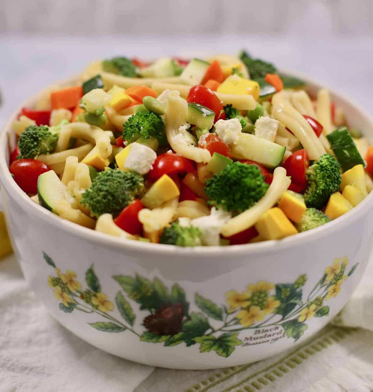 A large bowl with pasta salad and vegetables on a white and green napkin.