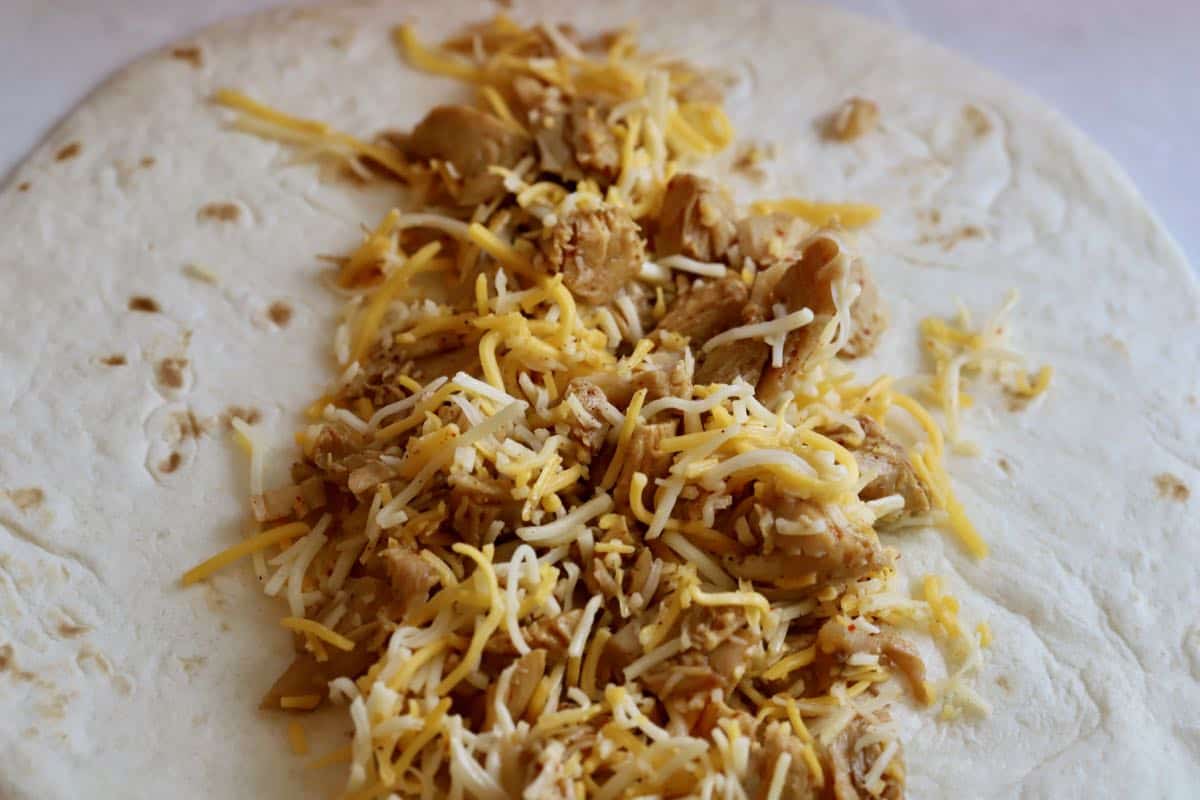 A flour tortilla topped with a mixture of chicken and cheese. 