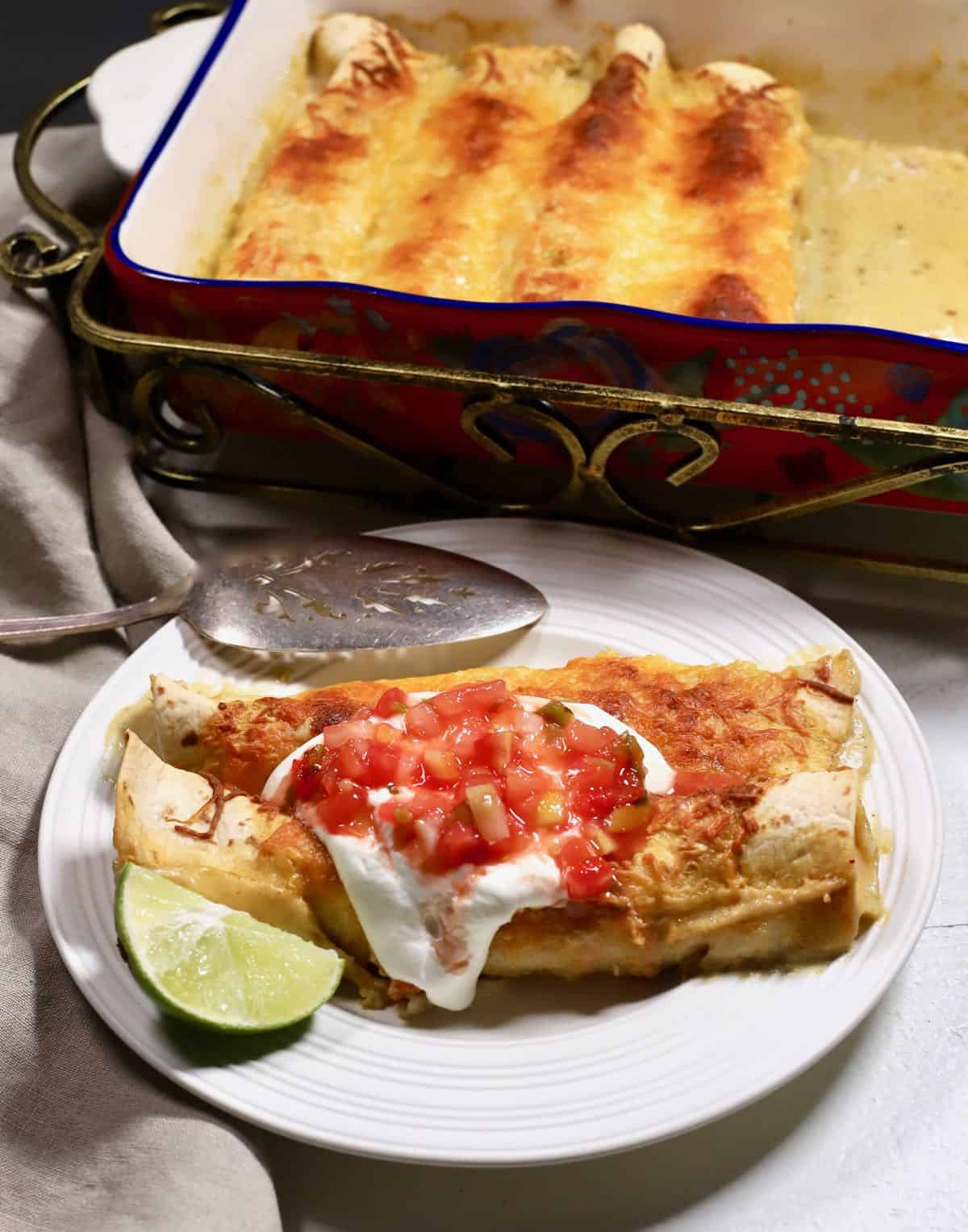 Enchiladas on a plate next to a baking dish full of them. 