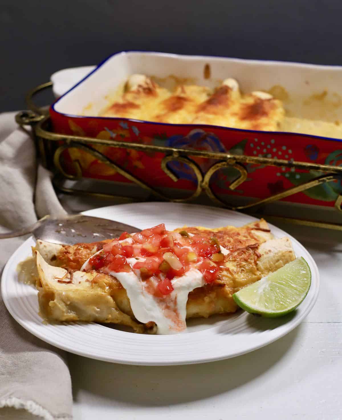 Two enchiladas on a plate topped with salsa and sour cream. 