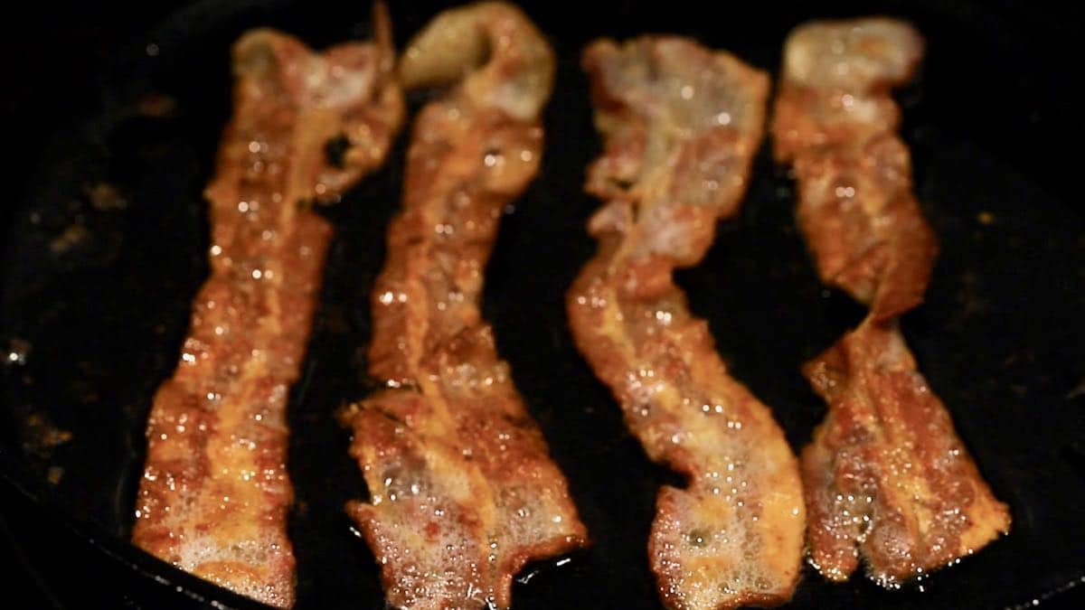 Four pieces of bacon cooking in a skillet. 