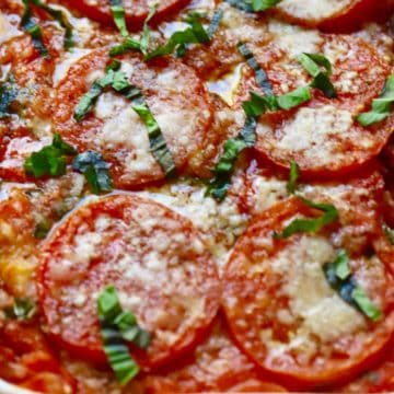 Baked tomato casserole topped with parmesan cheese and basil.