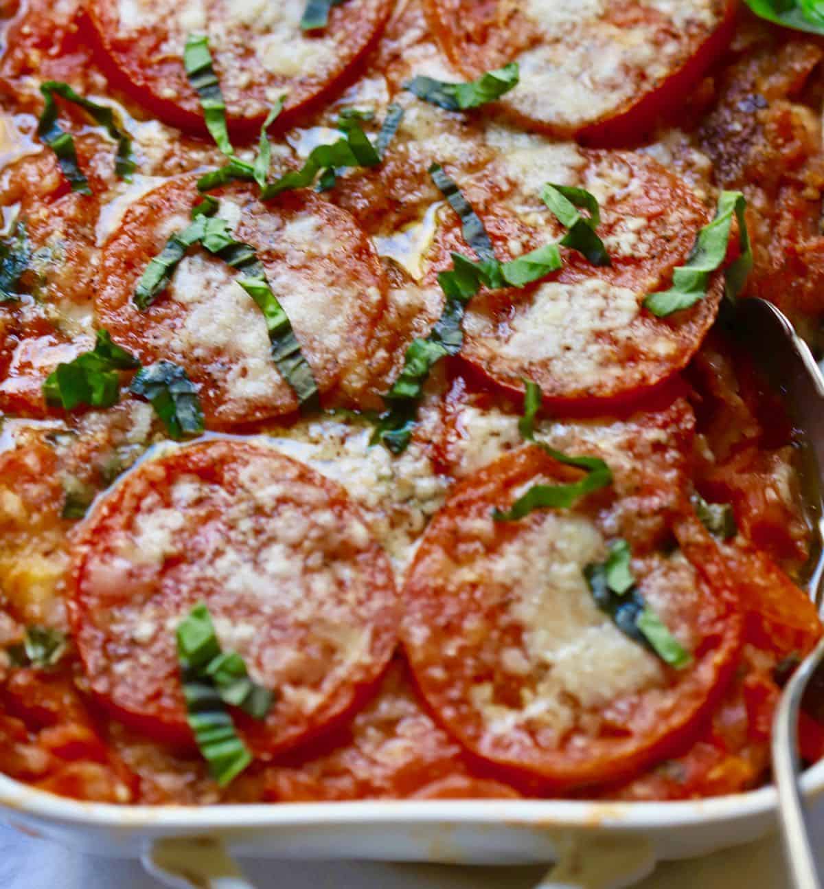 A white casserole dish with baked tomatoes topped with parmesan cheese and basil.