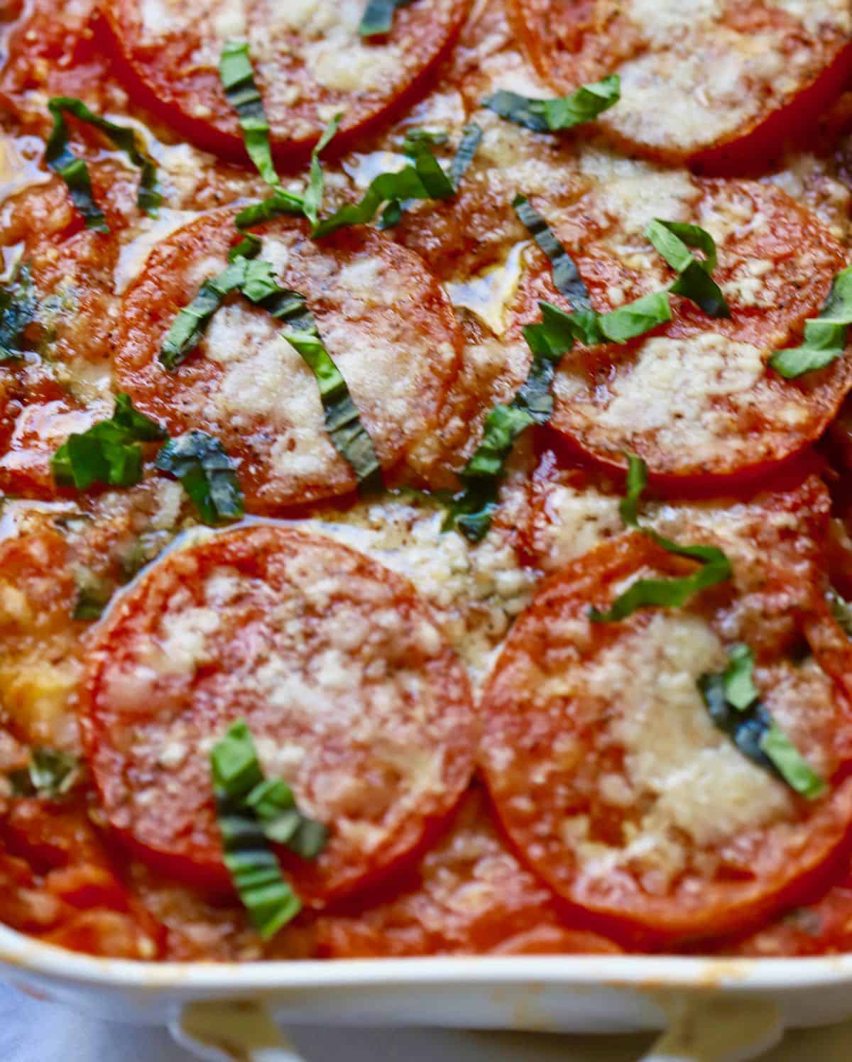 Fresh basil and parmesan cheese top a baked tomato casserole.